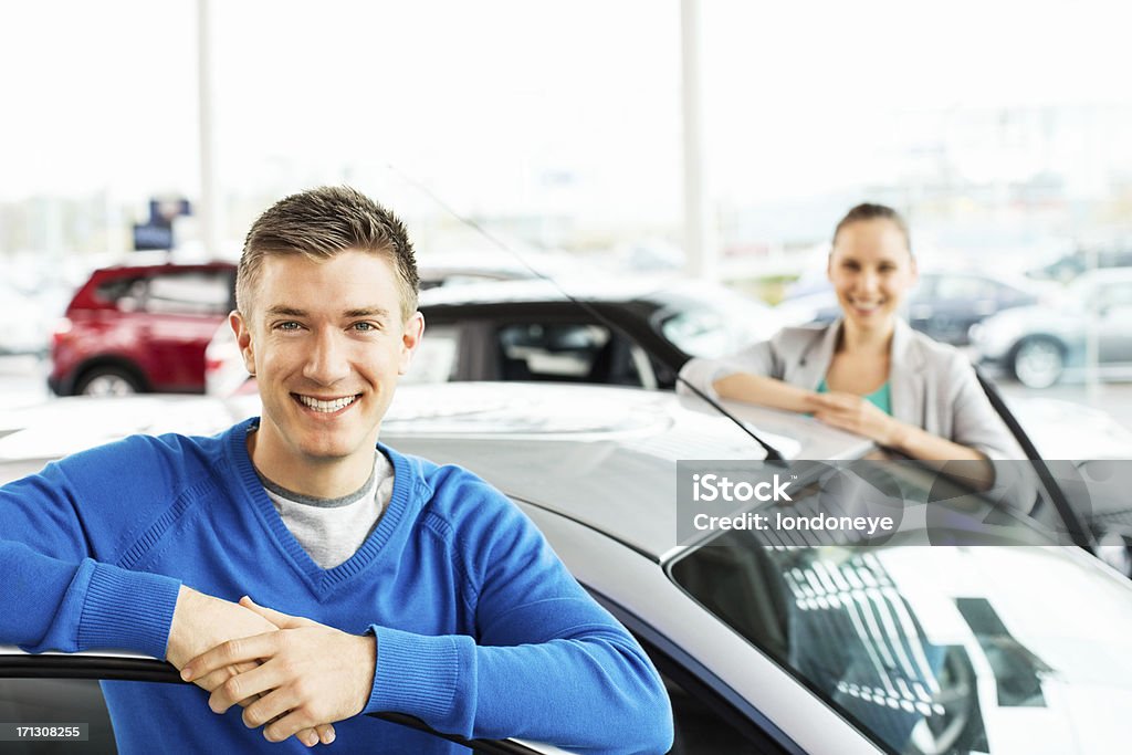 Happy Young Couple By New Car Portrait of a happy young man with girlfriend standing by new car at showroom. Horizontal shot. Dating Stock Photo