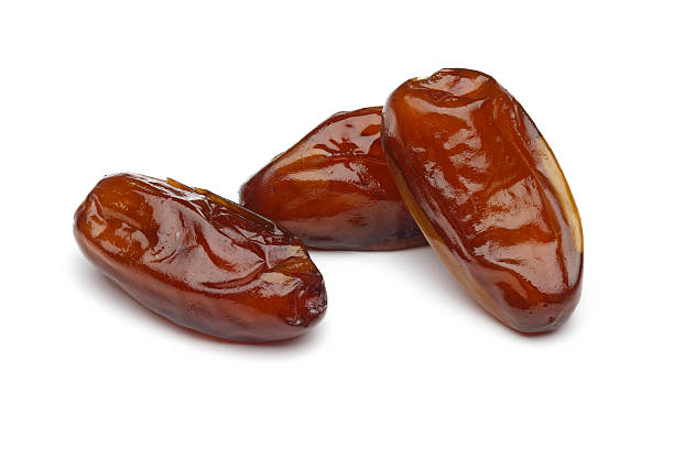 Three dried dates laying on a white surface stock photo
