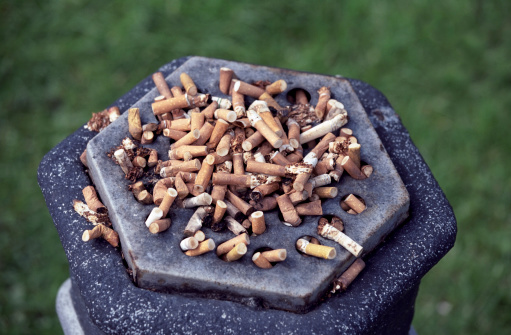 A public ashtray in a park, full of extincted cigarette ends.