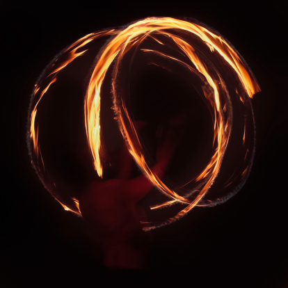 Closeup of a motion blurred fire dancer spinning poi at an outdoor music festival. Low light, high ISO.