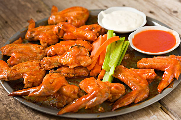 Hot Wings With The Works "Close up shot of a large tray covered with hot spicy Buffalo wings, some cruditAs (carrots and celery), a bowl of ranch dressing and a bowl with some fiery red hot sauce. Help yourself." tailgate party photos stock pictures, royalty-free photos & images