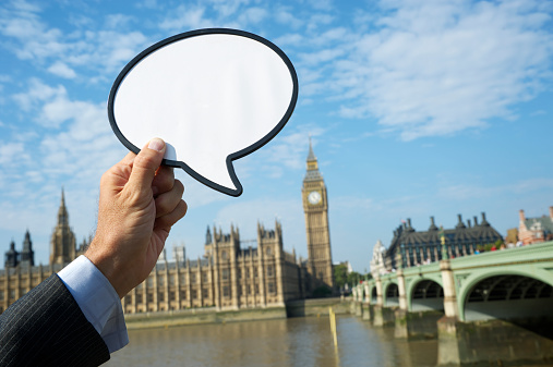 Hand of businessman holds speech bubble over Westminster Palace and Big Ben, London