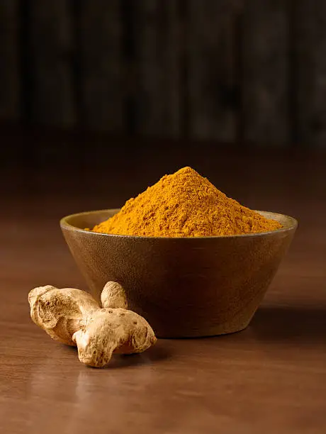 Bowl of Tumeric with Curcumin root on wood surface.  Rustic wood background.