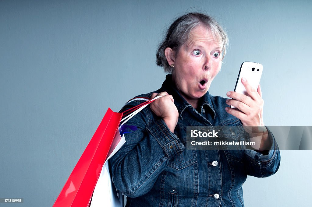 Пожилая женщина смотрит на ее смарт-телефон выходит удивленная - Стоковые фото 50-59 лет роялти-фри