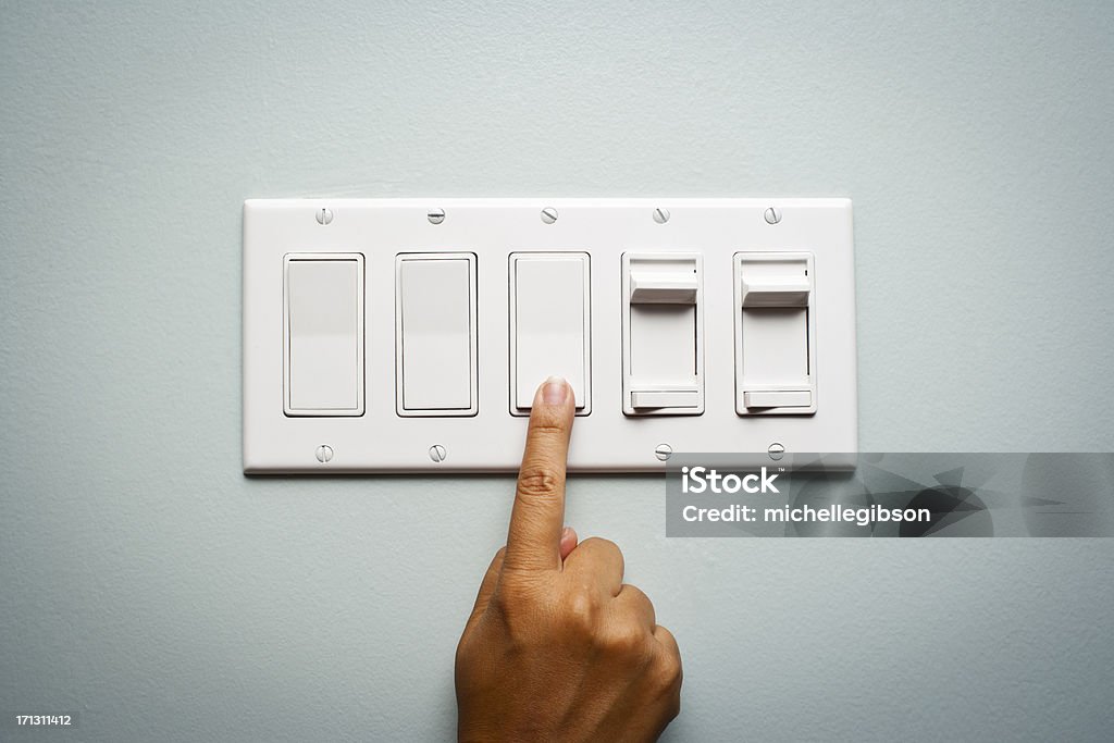 Woman's hand turning off the light Woman's hand on a light switch showing that she is turning off the power and electricity to conserve energy Turning On Or Off Stock Photo