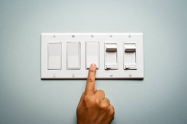 Woman's hand turning off the light Woman's hand on a light switch showing that she is turning off the power and electricity to conserve energy light switch stock pictures, royalty-free photos & images