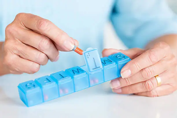 Cropped view of senior woman taking medicine from daily pill container. Horizontal shot.