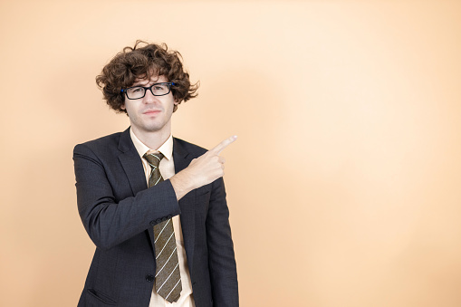 portrait cheerful young businessman wear spectacles in suit pointing finger pointing on empty blank copyspace to insert advertising text or articles satisfied on orange background.