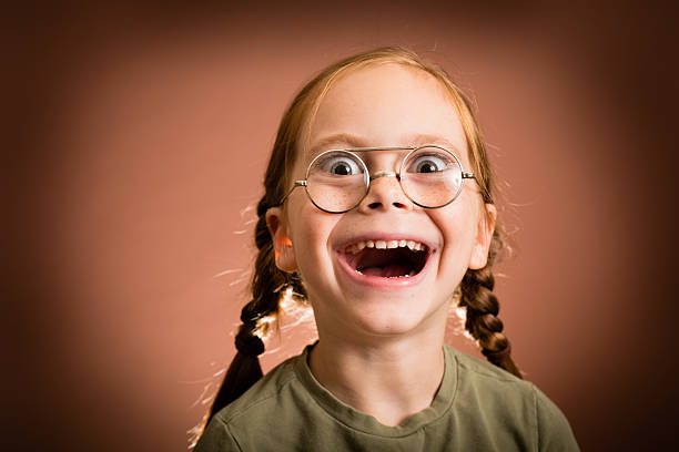 Happy/Excited Little Girl Wearing Nerdy Glasses "Color image of a young girl with red hair, wearing nerd glasses, with brown background." nerd kid stock pictures, royalty-free photos & images