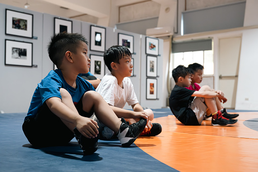 A gathering of school-age children sits along the sidelines, their faces filled with rapt attention as they absorb the wisdom and guidance shared by their dedicated sports coach.