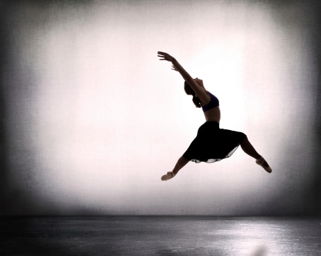 Female leaps across empty room in ballet shoes and skirt...backlit.