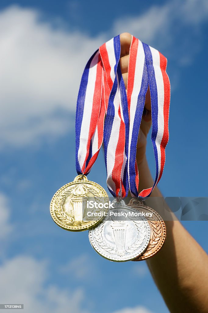 Gold Silver and Bronze Medals Hanging Hand Holding Blue Sky Hand holding up gold, silver, and bronze medals in bright blue sky International Multi-Sport Event Stock Photo
