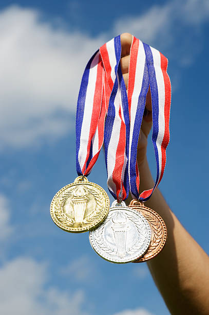 medalhas de ouro, prata e bronze penduradas mão segurando céu azul - unrecognizable person sky athlete competitive sport - fotografias e filmes do acervo