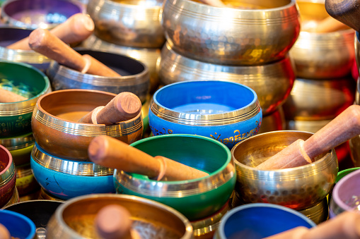 Many small singing bowls mti mallet, in different colors and partly with gold rim, partly stacked