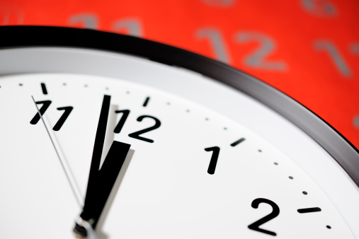 Close-up of Clock face of deadline against large red calendar.