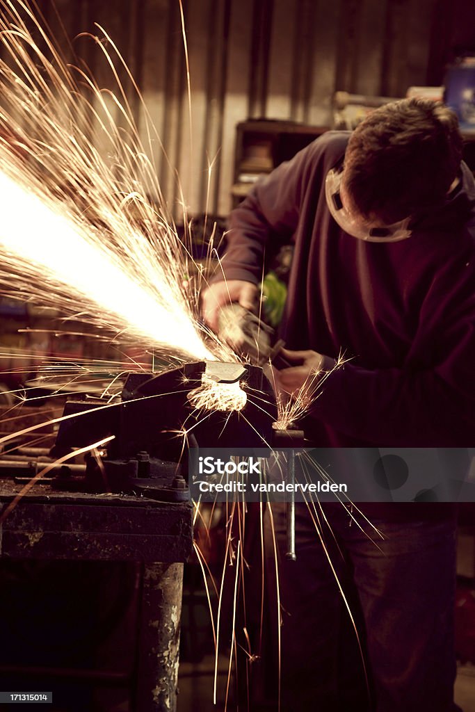 Sparks Fly From An Angle Grinder A workman wearing safety goggles operating a small angle grinder to sharpen a piece of metal held in a vice. Adult Stock Photo