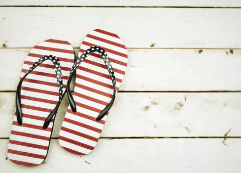 Pair of red, white and blue flip flops on white washed pine with vintage processing and texture added. Space at right for copy.