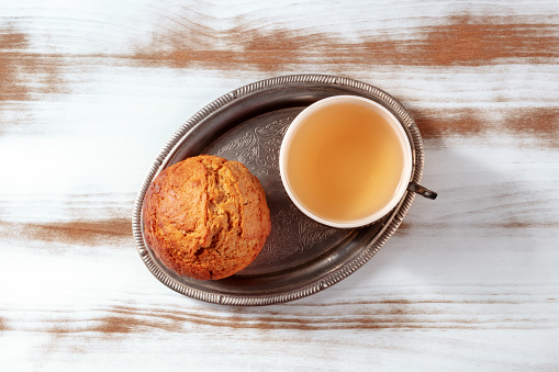 Orange muffin with tea on a rustic wooden kitchen table, on a vintage tray, overhead flat lay shot
