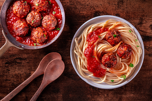 Meatballs. Beef meat balls, overhead flat lay shot in a pan and with a plate of spaghetti pasta, on a wooden background, with tomato sauce and wooden spoons