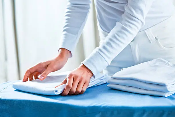 Close up of woman's hands stacking white folded and ironed t-shirts.