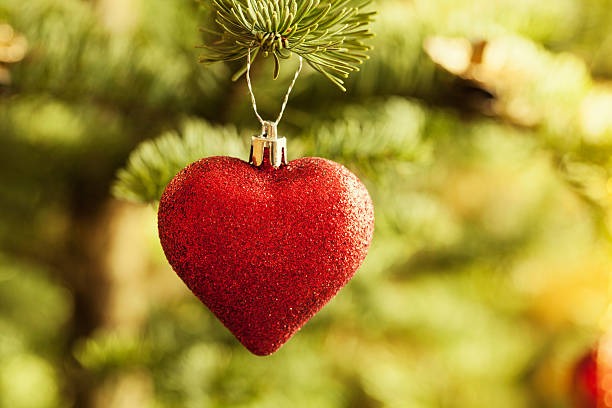 glittery christmas bauble in heart shape hanging in christmas tree