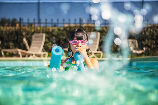 Little girl wearing goggles squirting water with a pool noodle.