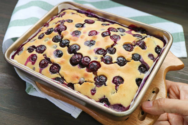 Hand Placing Freshly Baked Blueberry Cake on Kitchen Table