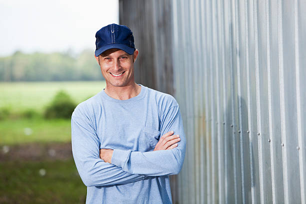 Smiling man (40s) wearing baseball cap standing outside building.