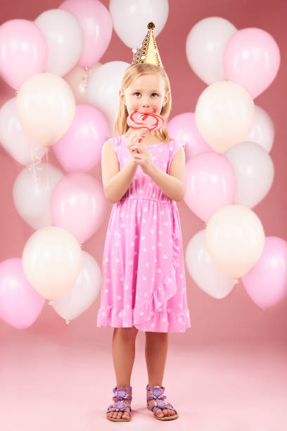 balloons, lollipop and portrait of girl in studio for birthday party, celebration and special day. happy, excited and young cute child smile with candy, sweet treats and dessert on pink background - celebration inflatable excitement concepts imagens e fotografias de stock