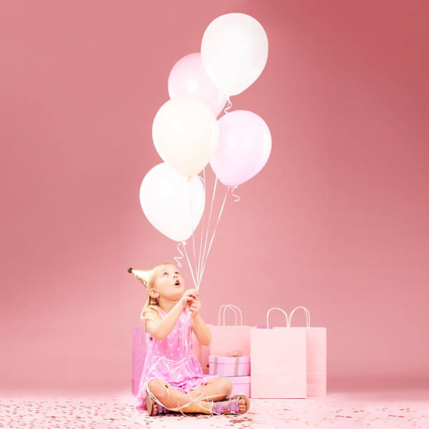 balloons, birthday and girl on pink background for celebration, party and special day in studio. happy, wonder and excited young child sitting with presents, gift box and decoration for festive event - celebration inflatable excitement concepts imagens e fotografias de stock