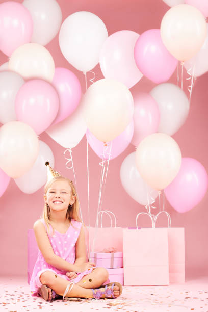 balloons, birthday and portrait of girl on pink background for party, celebration and special day. happy, excited and young child sitting with presents, gift box and decoration for event in studio - celebration inflatable excitement concepts imagens e fotografias de stock