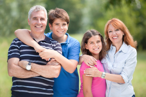 Portrait of happy mature couple with teenage kids smiling and looking at camera outdoor in park.