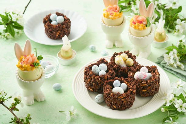 istock Easter chocolate nest cake with mini chocolate candy eggs with blossoming cherry or apple flowers on green background table. Creative recipe for Easter table with holiday decorations. Top view. 1713188734