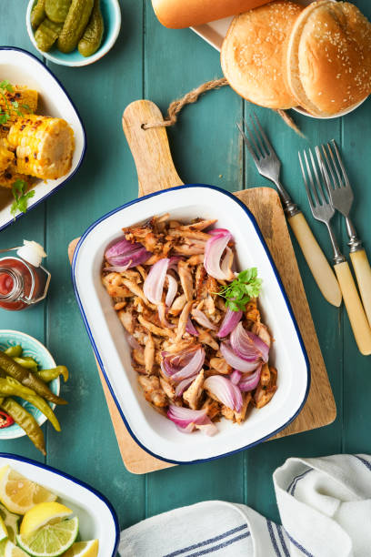 istock Pulled bbq chicken with baked onions on serving platter, bbq corn, pickles, chili peppers and buns for hot dogs and burgers, tomato sauce. Traditional American grilled summer bbq sandwiches dishes. 1713190411