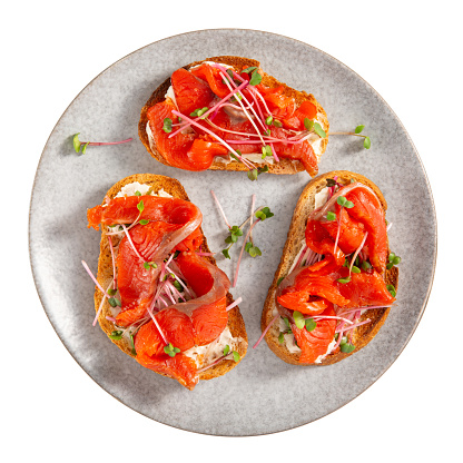 Sandwich with cream cheese, red salmon and microgreens on toasted bread. Three open sandwiches on gray plate isolated on white. Top view.