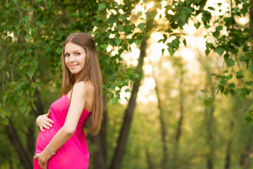 Beautiful pregnant woman in the park. Professional make-up and hairstyle.