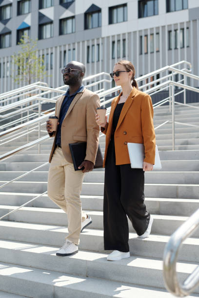istock Two young smiling colleagues carrying cups of coffee and gadgets 1713201037