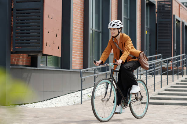 Young woman in formalwear and safety helmet sitting on bicycle stock photo