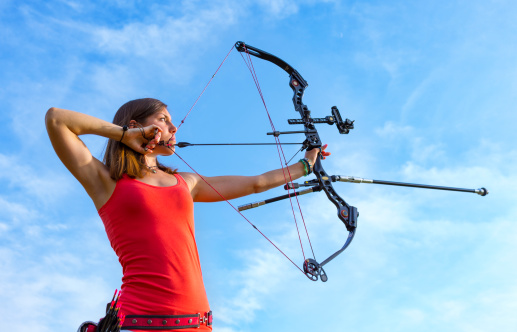 Young female adult, a professional archer aiming in position.