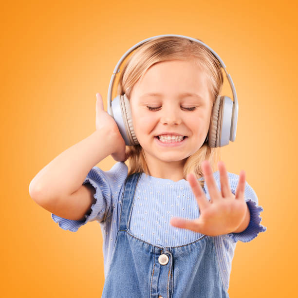 cuffie, balli o musica in streaming per bambini per rilassarsi con libertà in studio su sfondo arancione. sorridi, ragazza eccitata e felice che ascolta una canzone, un suono o un audio radiofonico su un abbonamento online - head in hands audio foto e immagini stock