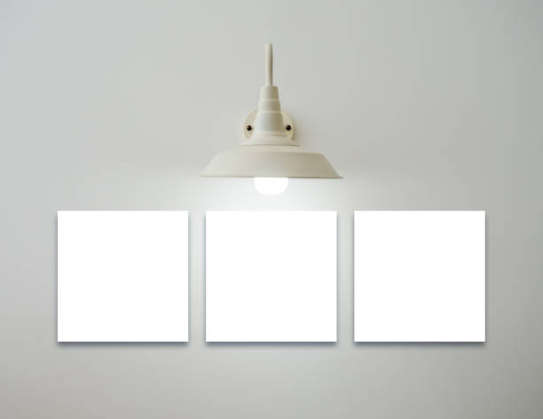 Mockup three square white blank picture frames set hanging under the vintage glowing light lamp on white background, minimal style. Template space for photography or painting decoration on the wall.