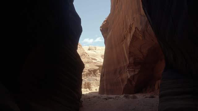 Tilt down handheld wide shot revealing a large opening from a hike through a tall orange sandstone slot canyon in buckskin gulch in southern Utah near Arizona on a warm sunny spring morning