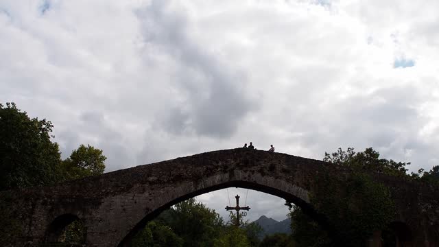 Tilt up Roman bridge, Puente Vieyu or Puenton, historic site in Cangas de Onis, Asturias, Spain. Tourist landmark monument over Sella river. Romanesque style with arches and the Victory Cross hanging.