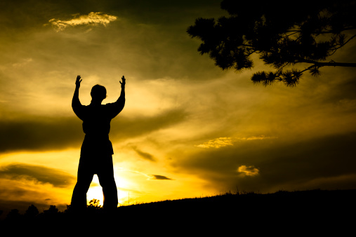 Silhouette of person arms raised in praise at sunset.  