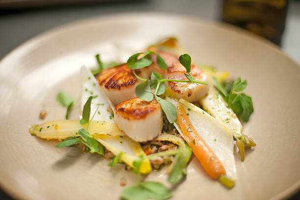 Scallops on a plate with watercress, endive, and baby carrots stock photo