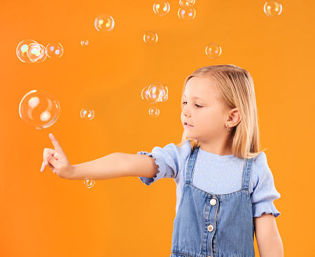 Young girl child, pop bubbles and game, playing and fun with youth isolated on orange background. Liquid soap, development with kid from Australia in studio, playful and toys with childhood