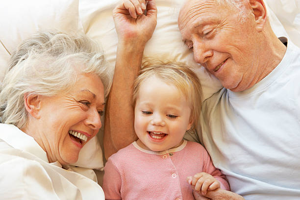 abuelos abrazarse granddaughter en la cama - abuelo y bebe fotografías e imágenes de stock
