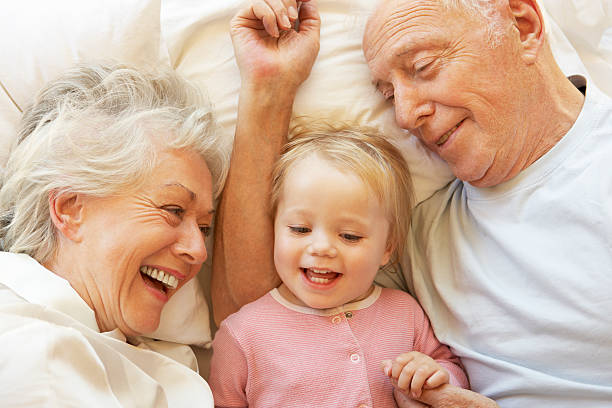 Grandparents Cuddling Granddaughter In Bed Happy Smilling Grandparents Cuddling Granddaughter In Bed. old man pajamas photos stock pictures, royalty-free photos & images