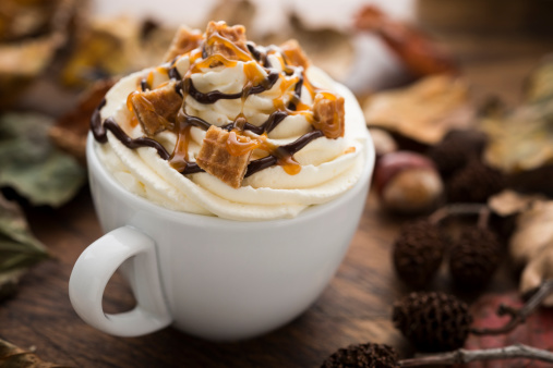 Hot drink (hot chocolate or Flavoured Coffee) with Whipped Cream, Caramel Waffle pieces, caramel sauce and Chocolate sauce, surrounded by dried Autumn Leaves.