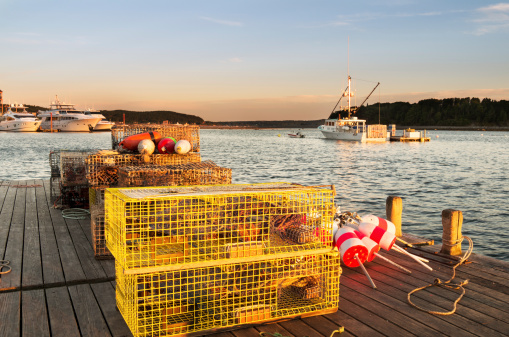 Pier in Maine Harbor with lobster traps in foreground and Lobster boats in background.